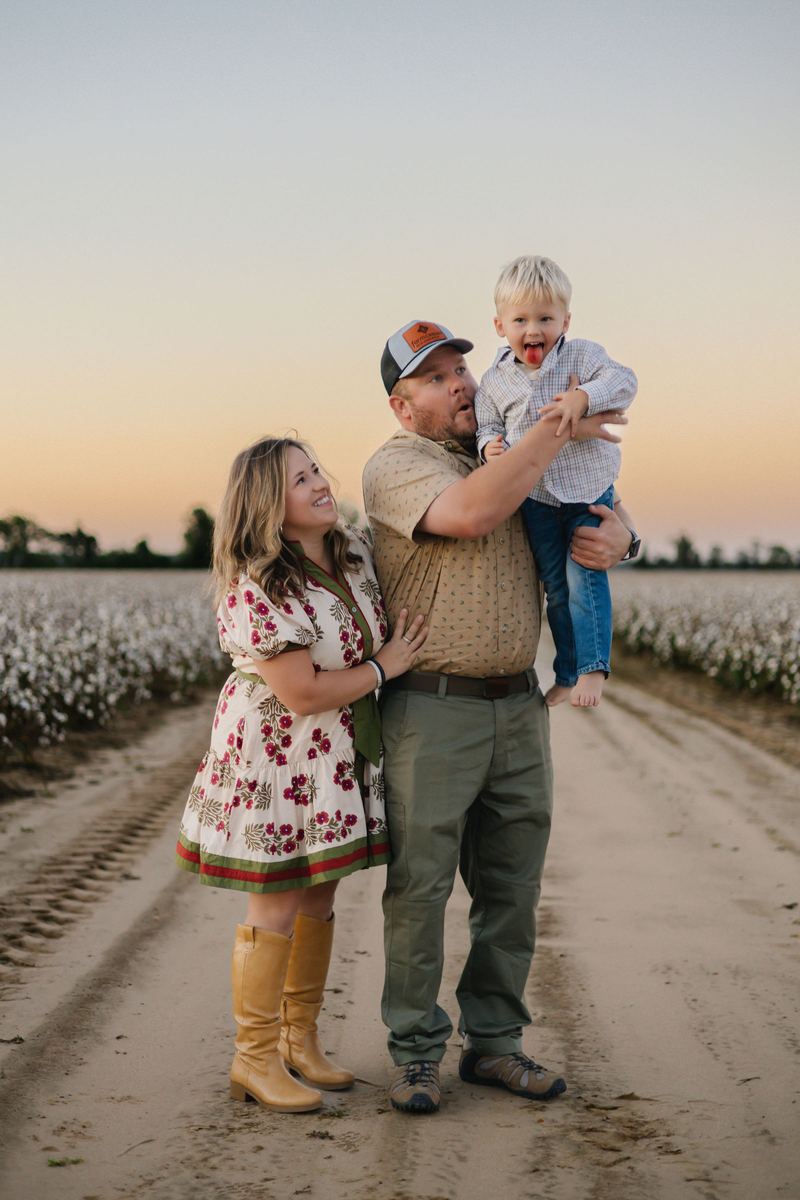 Family of three walking down a cotton-field road at sunset