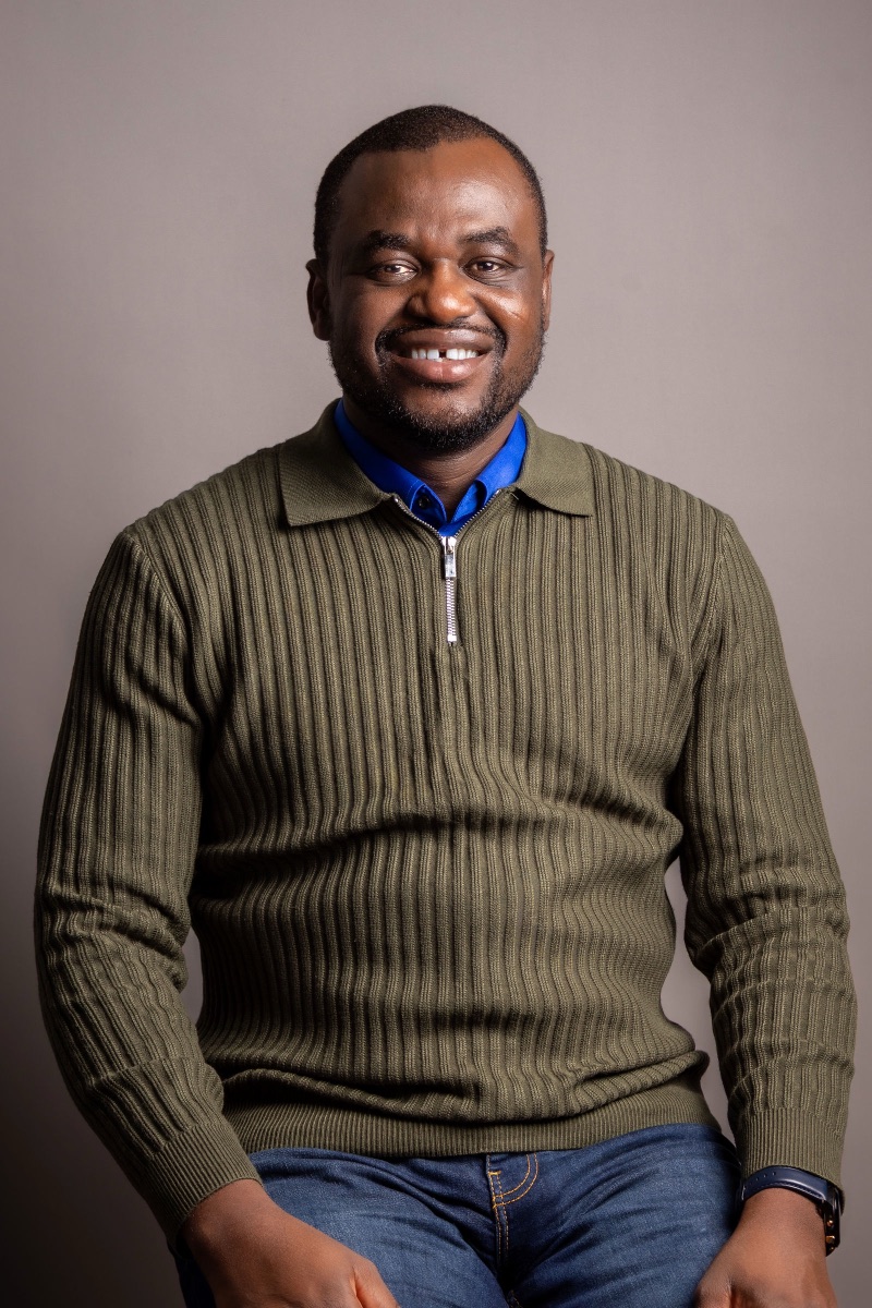 Studio headshot of a man laughing in a green quarter-zip sweater
