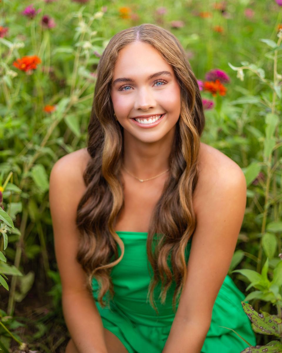 Senior girl in a green dress smiling among wildflowers