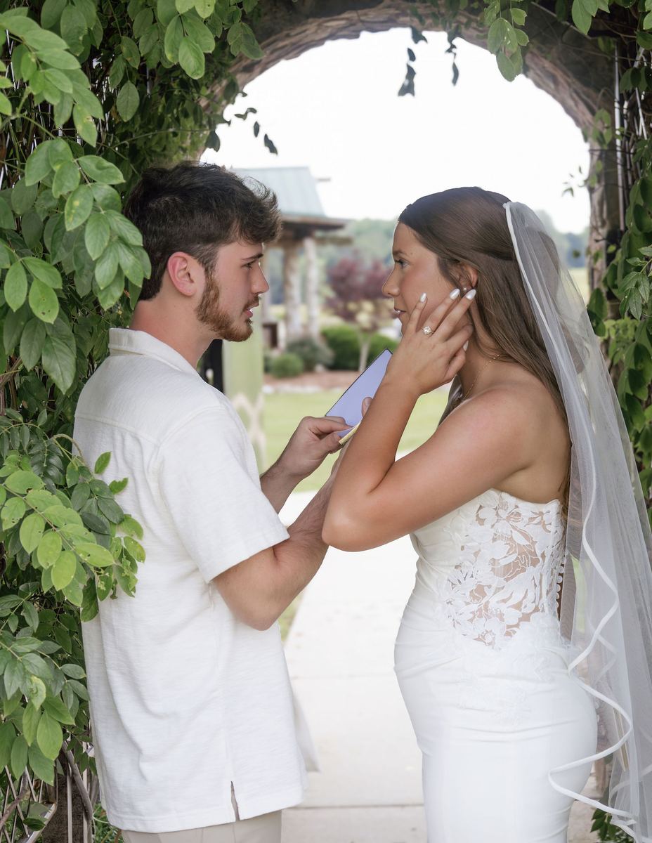 First look: groom cupping the bride's face under a vine arbor