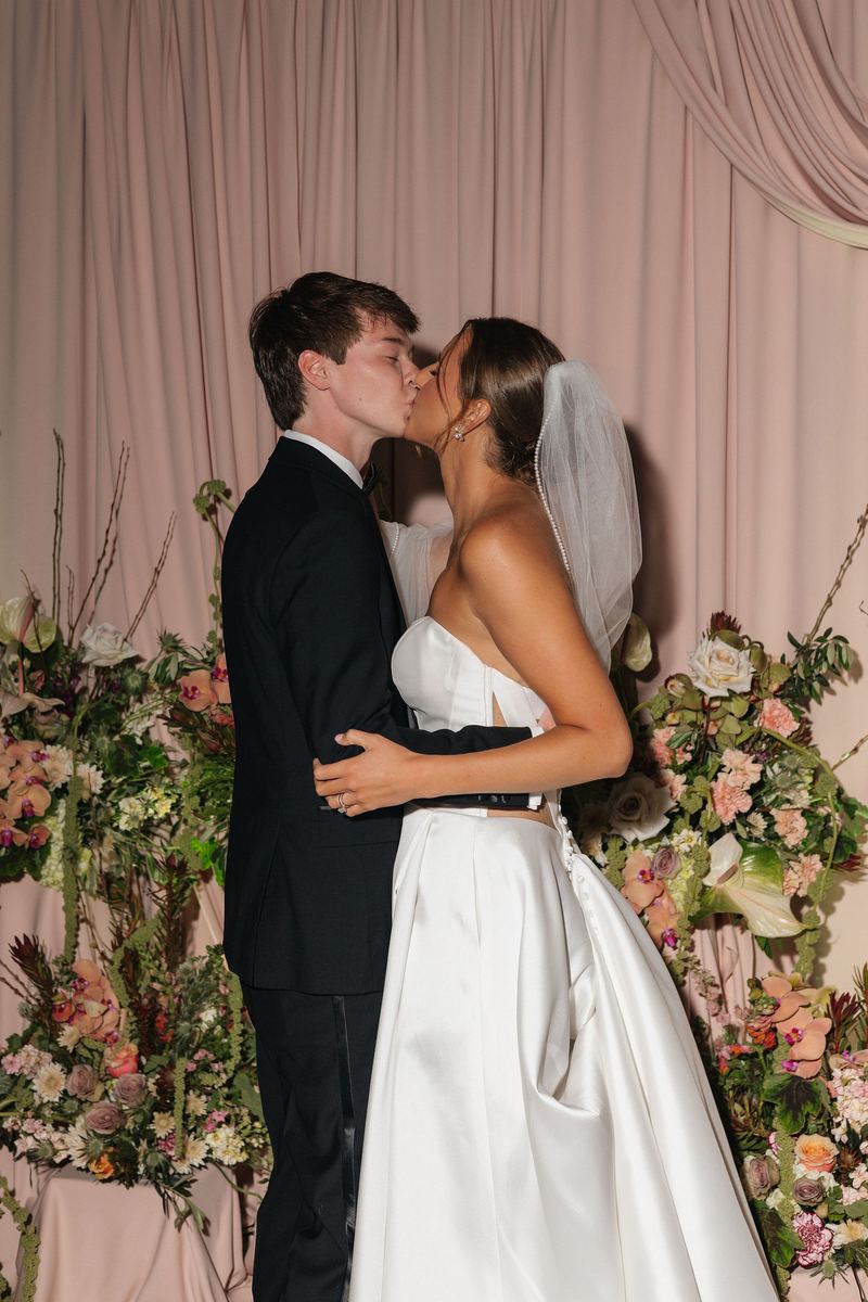 Bride and groom kissing in front of blush drapes and flowers